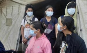 Three girls and two boys standing, wearing a mask
